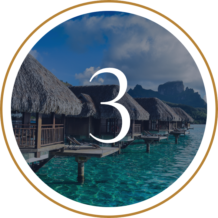 Overwater bungalows with thatched roofs on clear turquoise water, mountain landscape in the background, clear sky with some clouds.