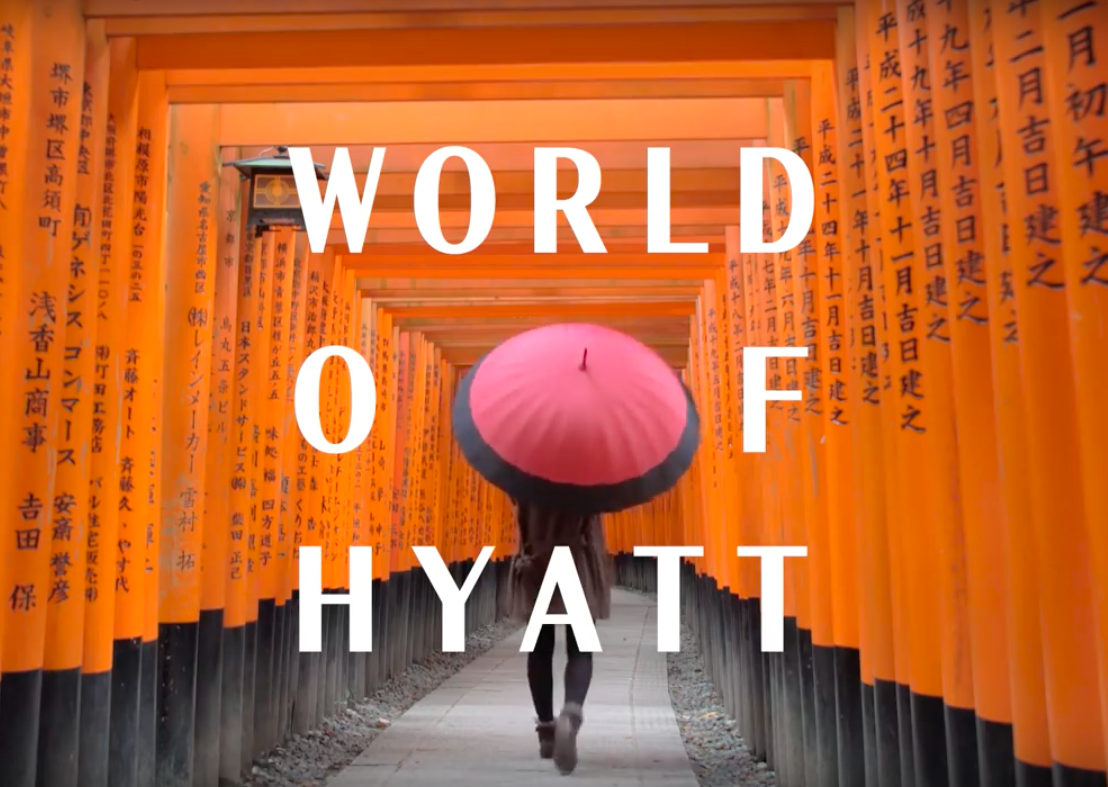 A person walking through a pathway lined with orange torii gates with Japanese writing, holding a pink and black umbrella.