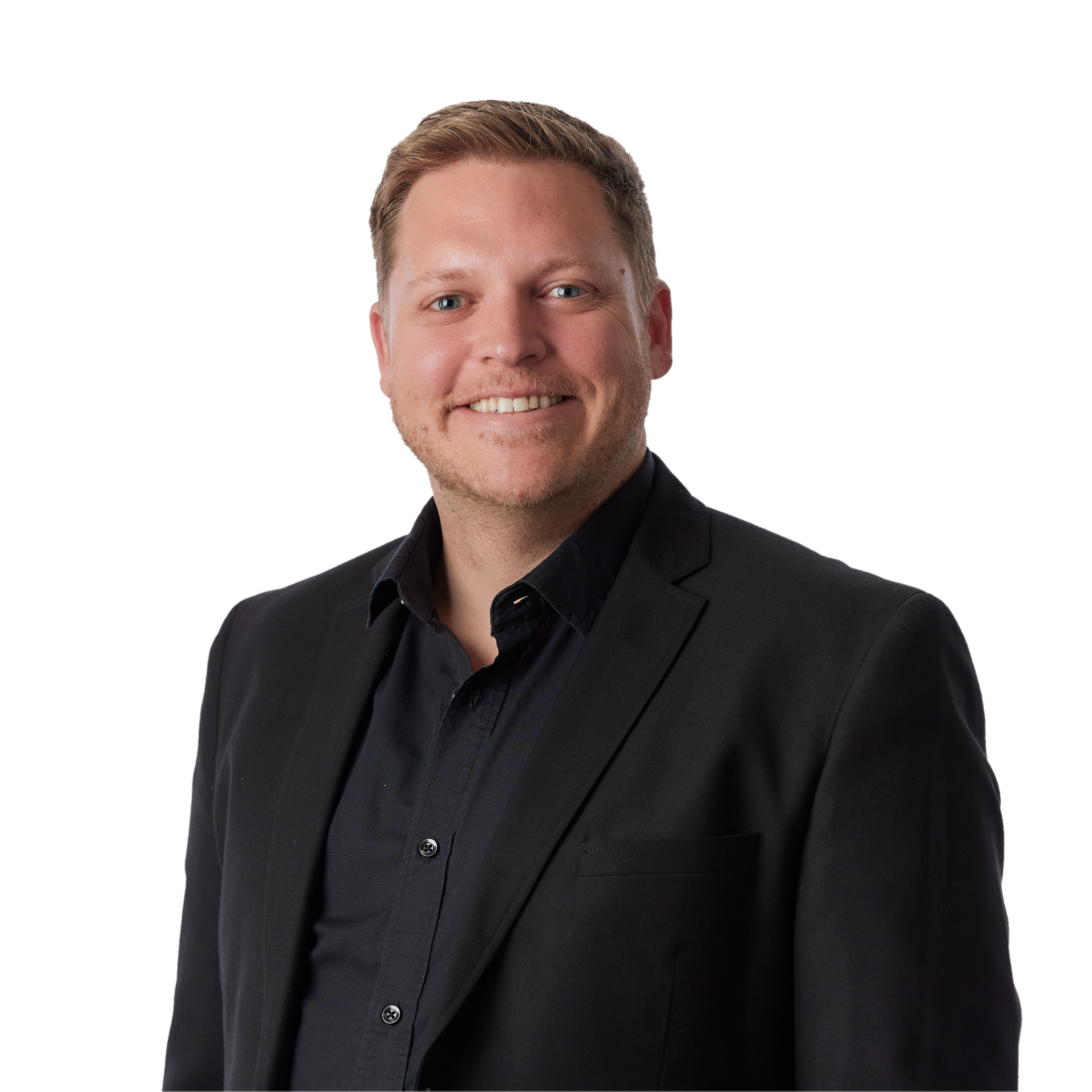 Close-up portrait of a smiling man with blond hair, blue eyes, and light facial hair, dressed in a black suit and black shirt.