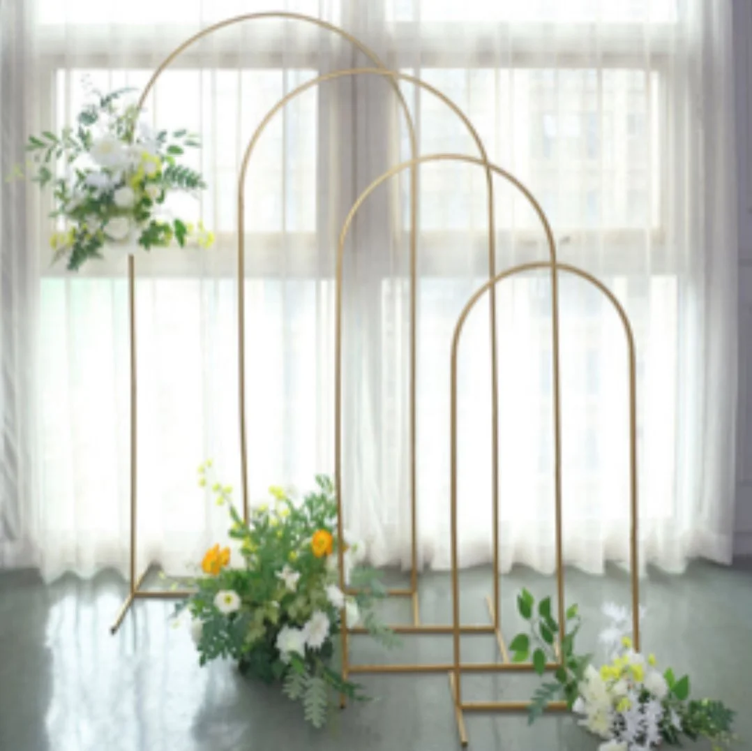 Decorative gold metal arches with floral arrangements of white, yellow, and green flowers near a window with sheer white curtains.