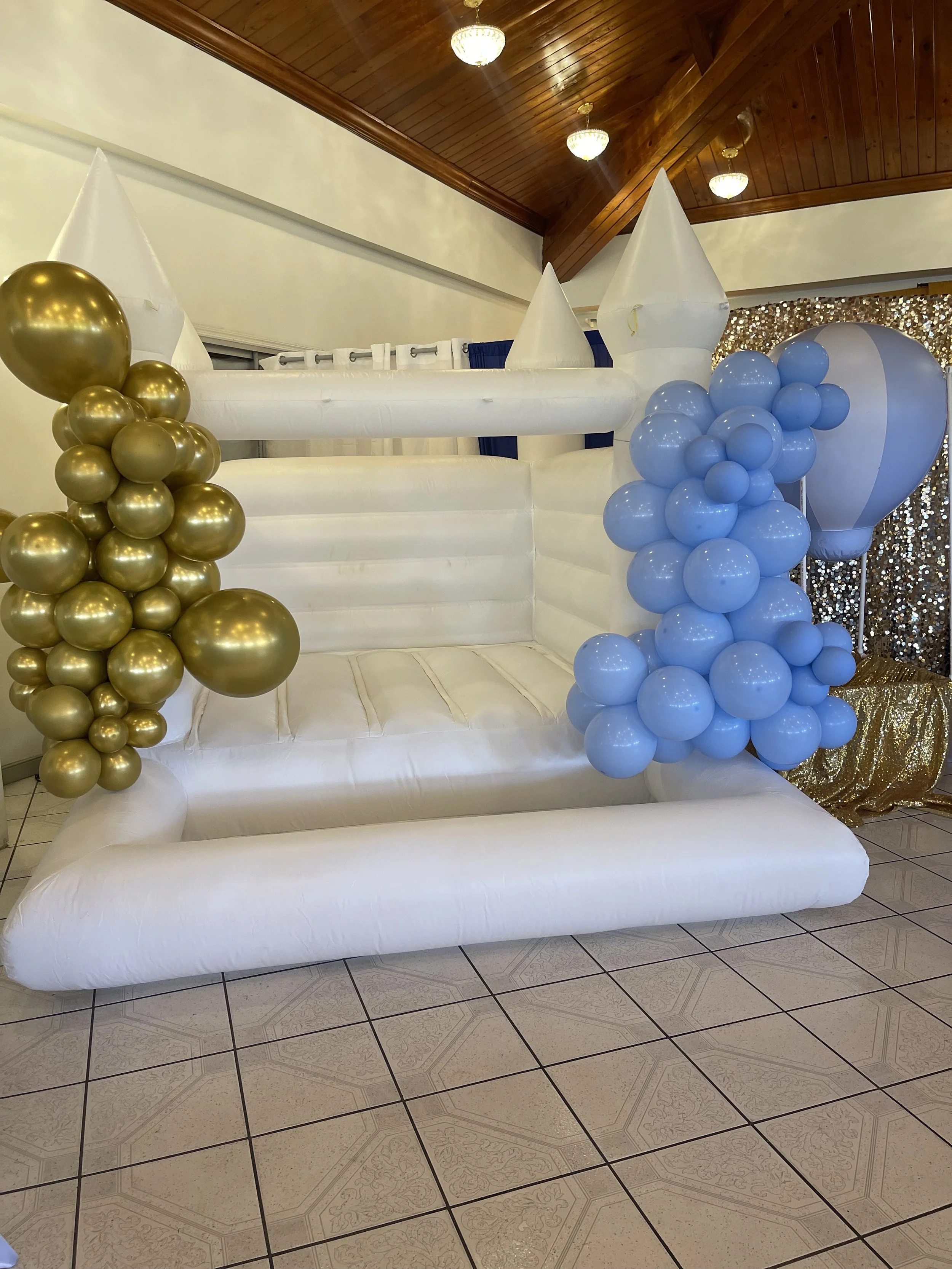Decorated white float with gold and blue balloon clusters, white coned structures, and a backdrop of gold and silver sequin fabric.