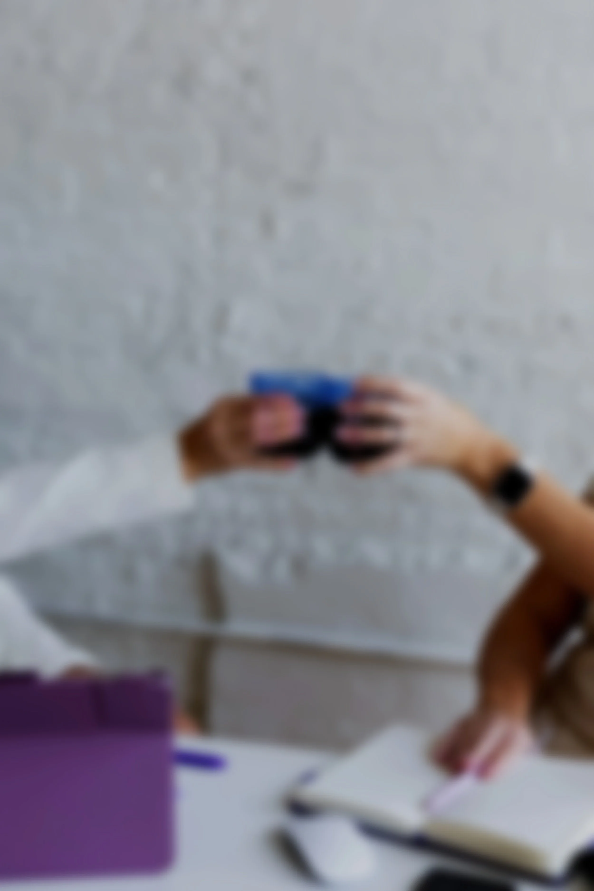 A person holding a small blue object in their hand, with a blurred background that includes a purple object and some other items.