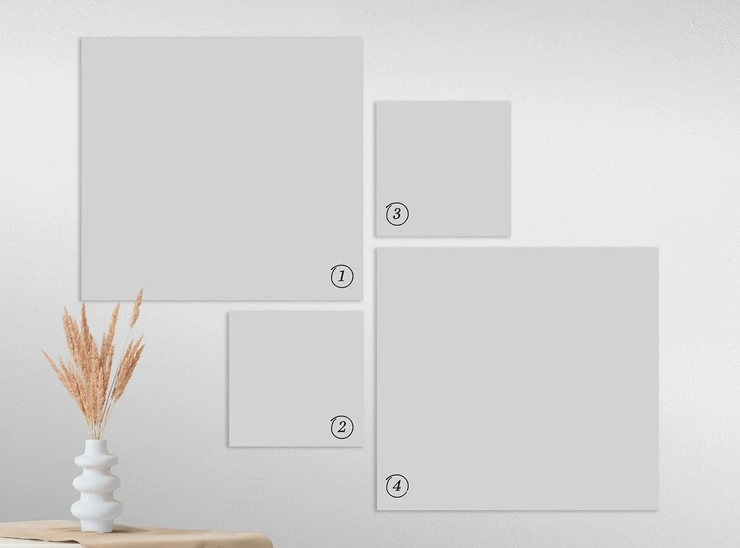 Wall with four blank picture frames and a white vase with beige dried flowers on a wooden table.