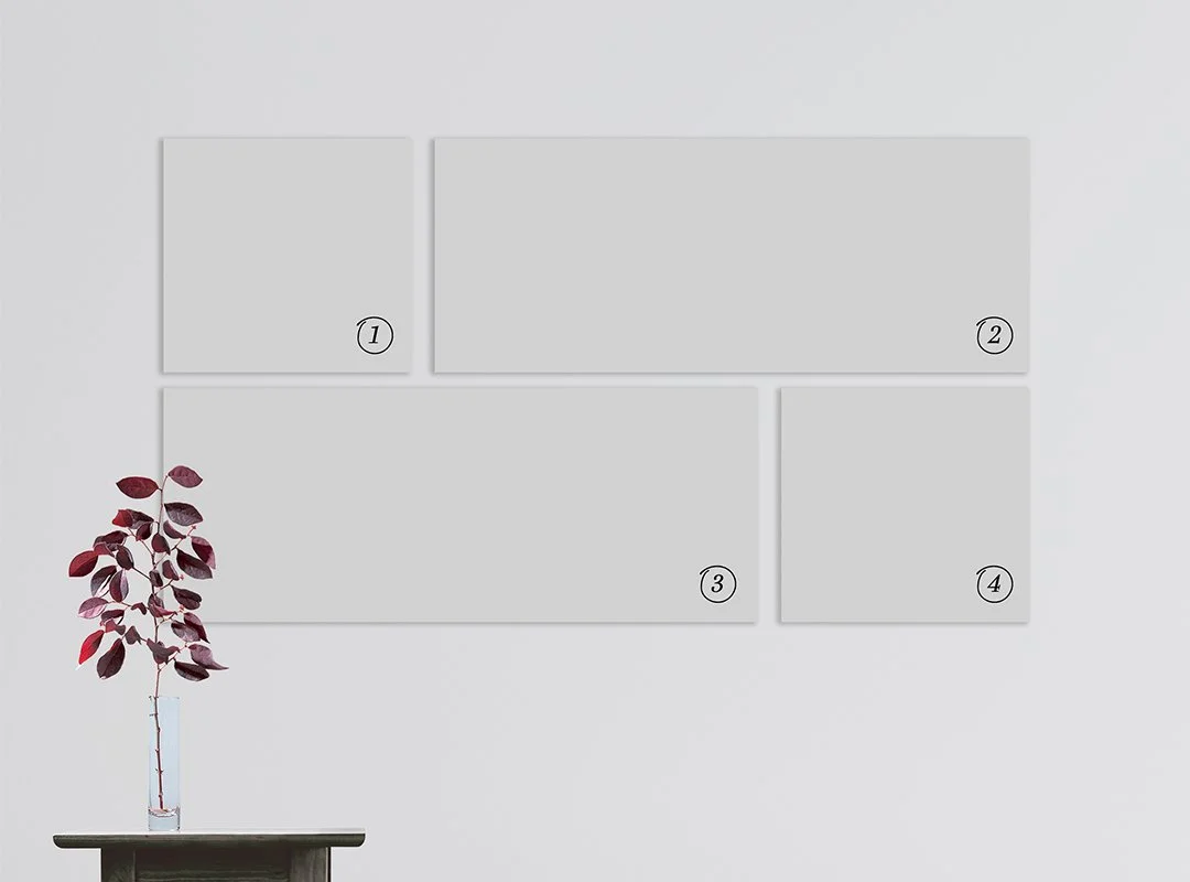 Four blank white rectangular canvases labeled 1, 2, 3, and 4 are hung on a white wall behind a small table with a vase containing dark red leaves.