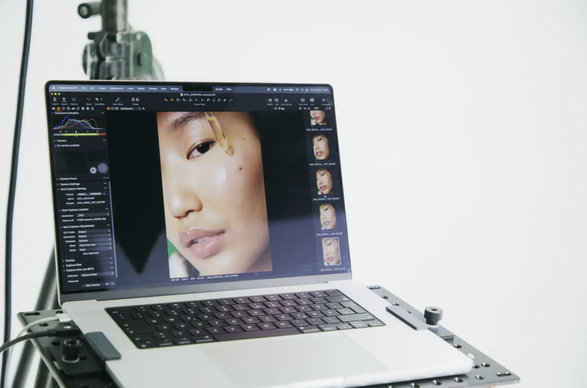A laptop on a stand displaying a close-up portrait of a woman's face during a photo editing session. The laptop screen shows photo editing software with adjustments and thumbnail images on the right.