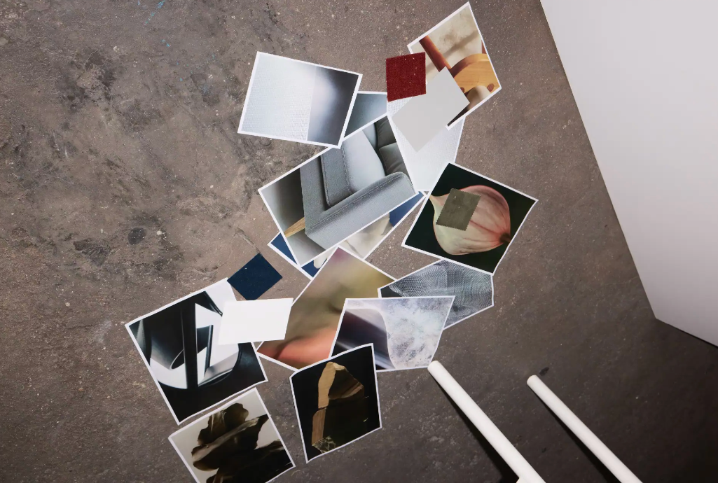 A collection of photographs and fabric swatches scattered on a concrete floor with white legs of furniture visible.