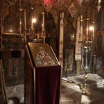 A religious altar inside a church with lit candles, an icon, and floral decorations.