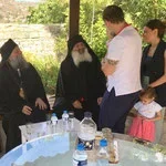 People standing outdoors near a table with water bottles and cups, engaging in conversation under trees.