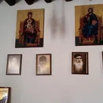 Wall with six framed pictures and religious artwork, including two large religious icons at the top and four smaller portrait-style frames below.