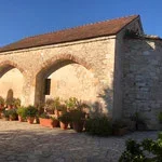 Stone building with an archway and potted plants outside under a clear blue sky.