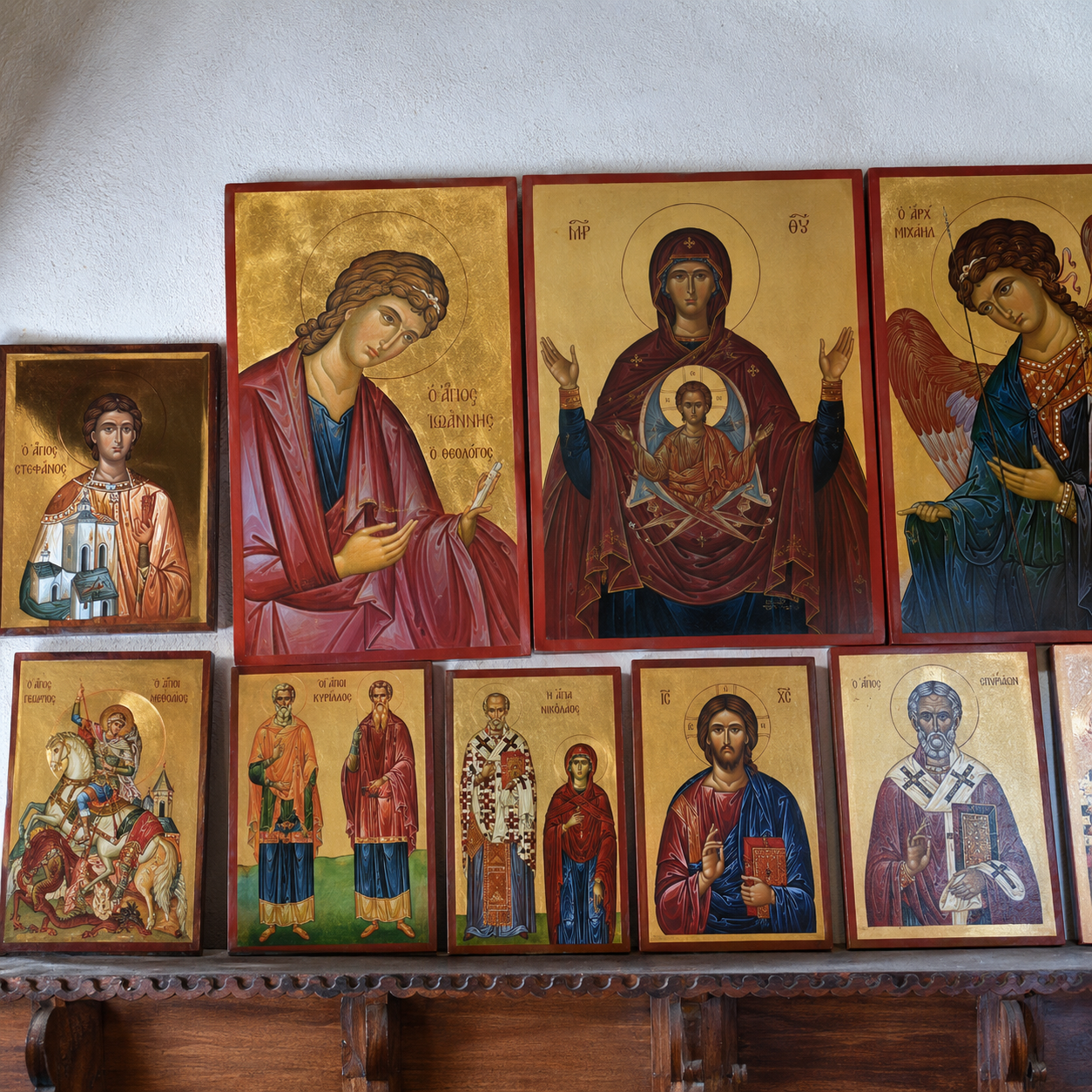 A collection of Christian icon paintings on a wooden shelf, depicting saints, the Virgin Mary, and Jesus Christ with gold backgrounds, in a traditional Orthodox style.