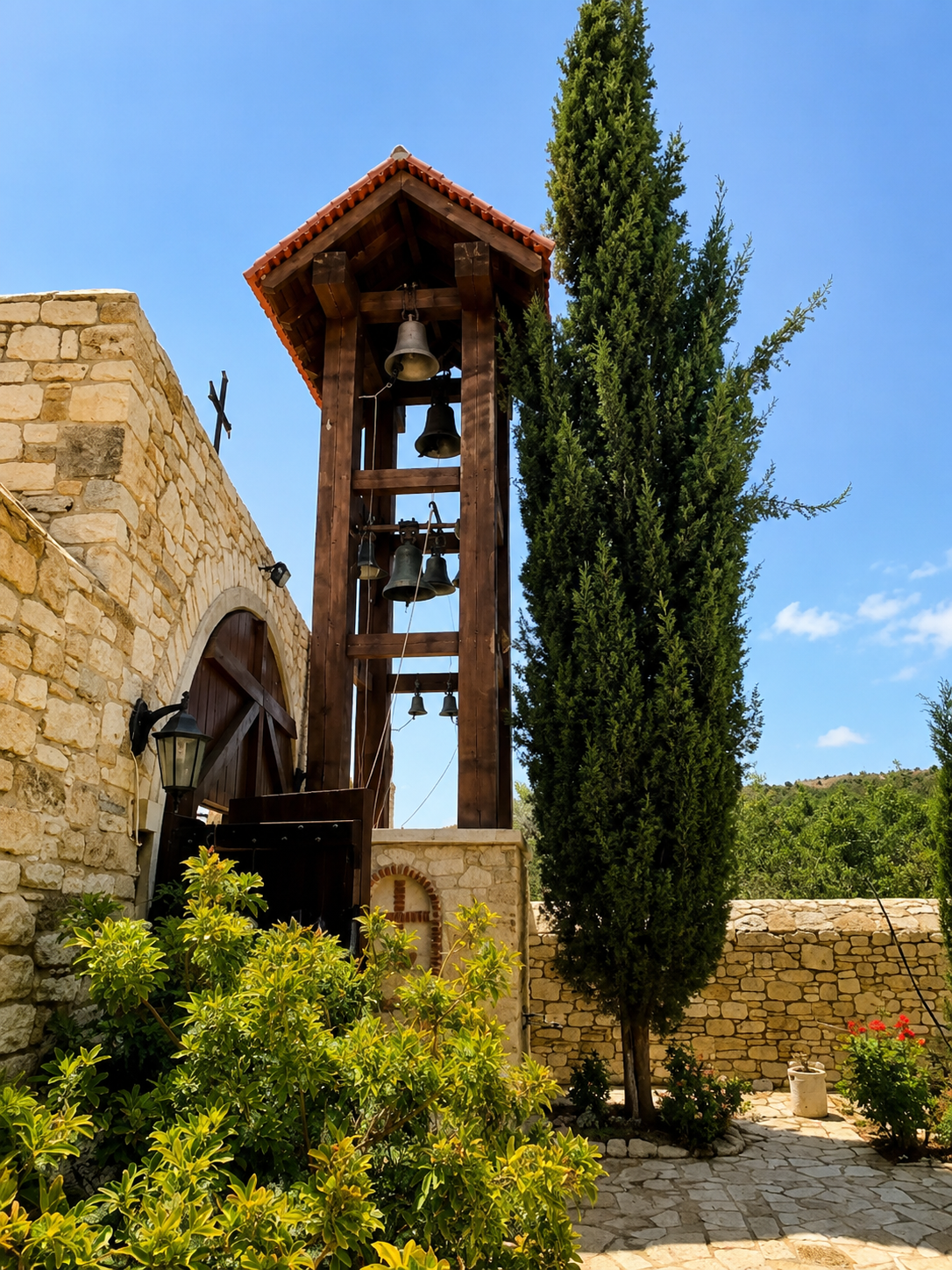 A stone building with a wooden bell tower and a tree in a courtyard with potted plants.