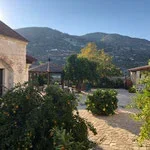 A rural village scene with stone buildings, trees, and mountains in the background.