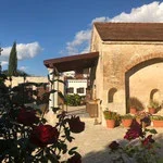 A building with a stucco exterior and a tiled roof, surrounded by flowers and trees under a blue sky with clouds.