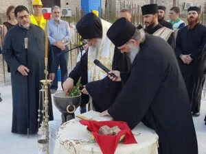 A group of men, some wearing traditional religious attire, gathered outdoors around a table with religious objects, participating in a religious ceremony or ritual.