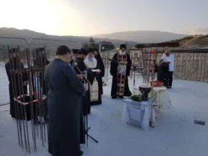 Group of people participating in a religious or memorial ceremony outdoors, with a mountain landscape in the background, some individuals praying or reading.