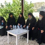 Group of five religious women wearing black clothing and head coverings sitting outdoors around a white table with water bottles.