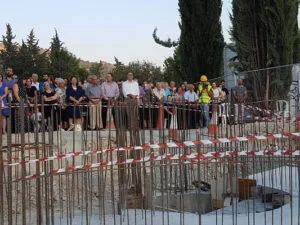 A group of people observing a construction site or something undergoing excavation, separated by orange and white safety tape.