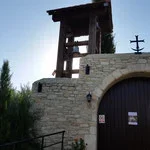 A stone building with a small bell tower or structure on top, set against a blue sky with some clouds and greenery.