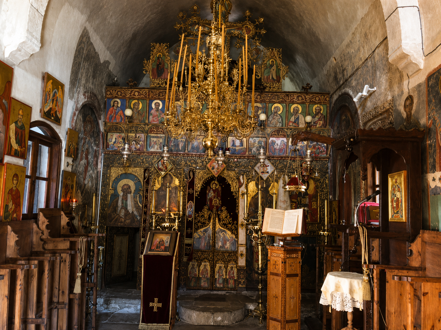 Interior of an Orthodox Christian church with religious icons, a large gold chandelier, and an altar with a gold and black iconostasis.