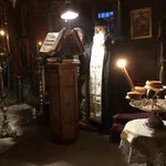 A dimly lit interior with a vintage cash register on a wooden table, a lit candle, and a window with light shining through, suggesting an old-fashioned or cozy setting.