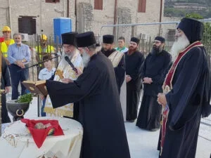 Religious ceremony with a group of Orthodox Jewish men, some wearing hats and prayer shawls, standing outdoors around a table with religious items.