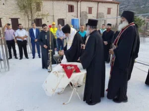 People participating in a religious or cultural ceremony outdoors, with some dressed in traditional attire and others in formal wear, gathered around an altar or table covered with a white cloth.