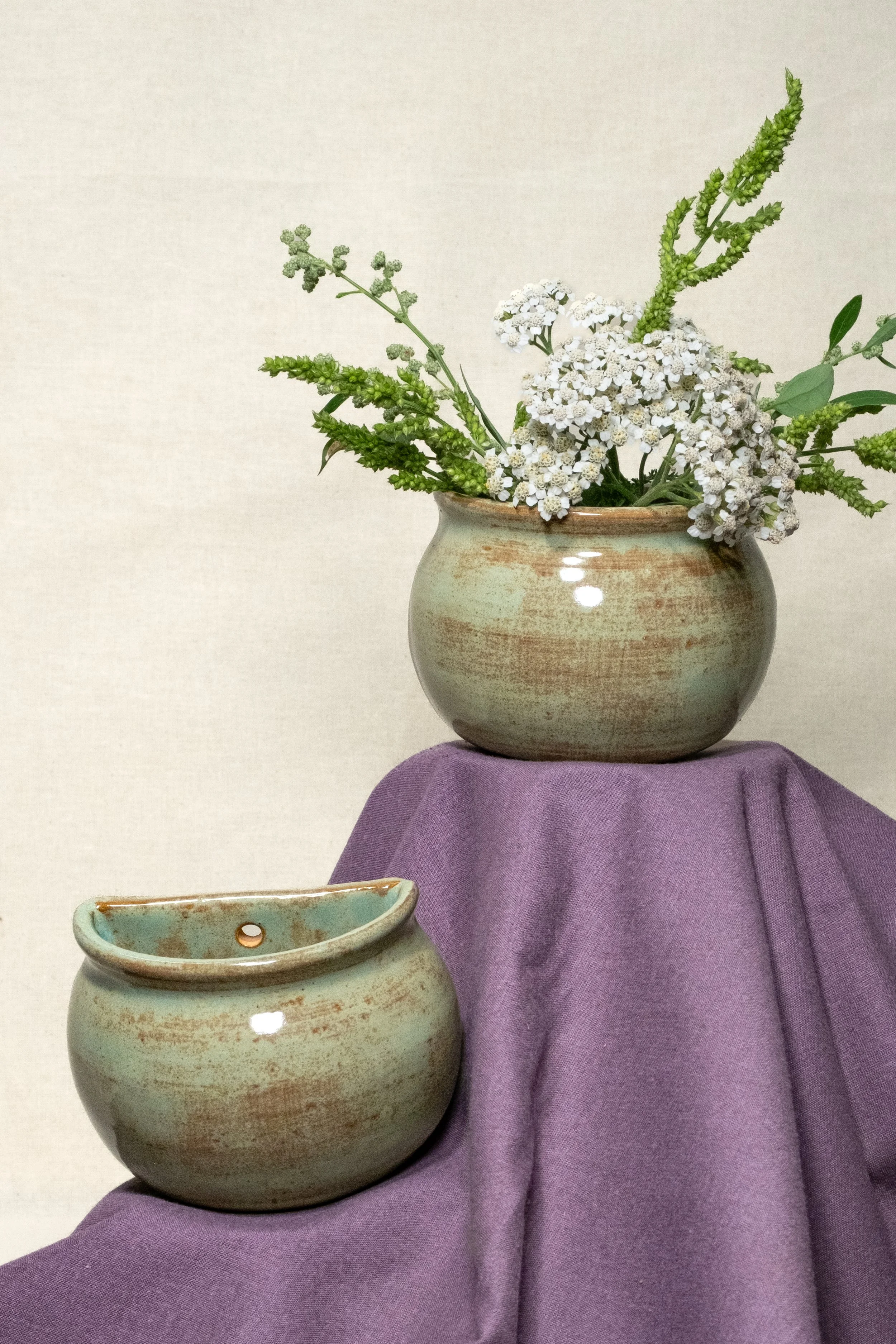 A ceramic vase with white and green flowers on a purple cloth.
