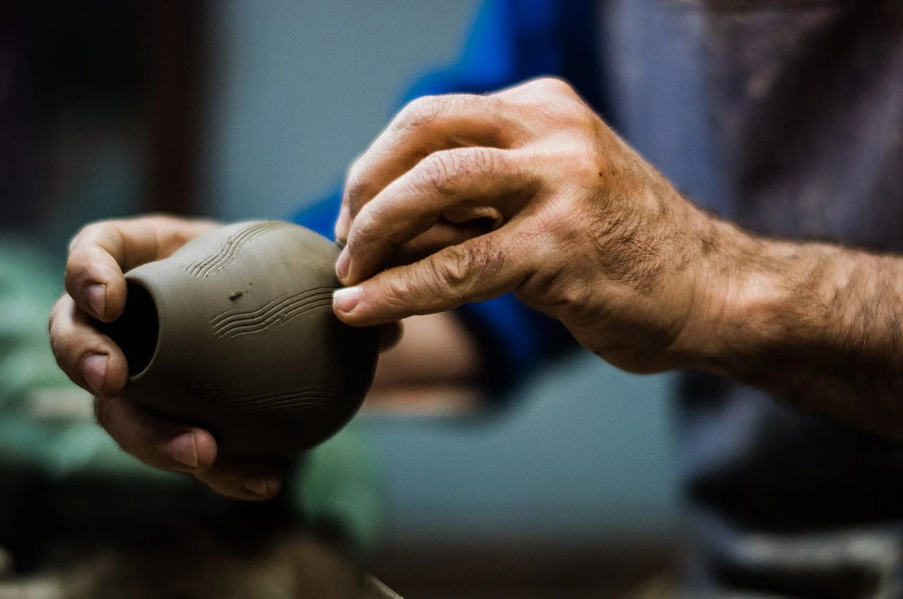 Hands shaping a small clay pot in a pottery workshop.
