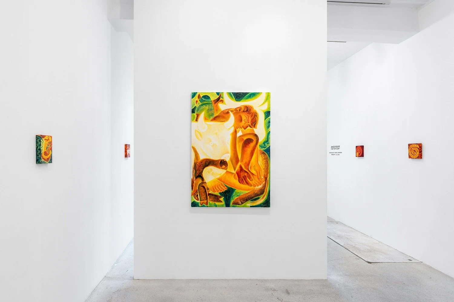 Art gallery with white walls displaying a large central painting of a stylized human figure with bright, warm colors and abstract background, and smaller paintings on either side.