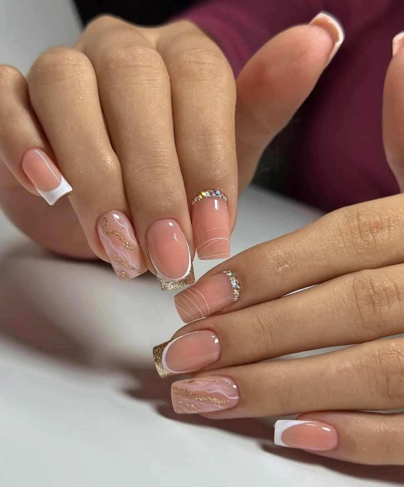 Close-up of hands with manicured nails featuring French tips, glitter accents, and a marble design with crystals.