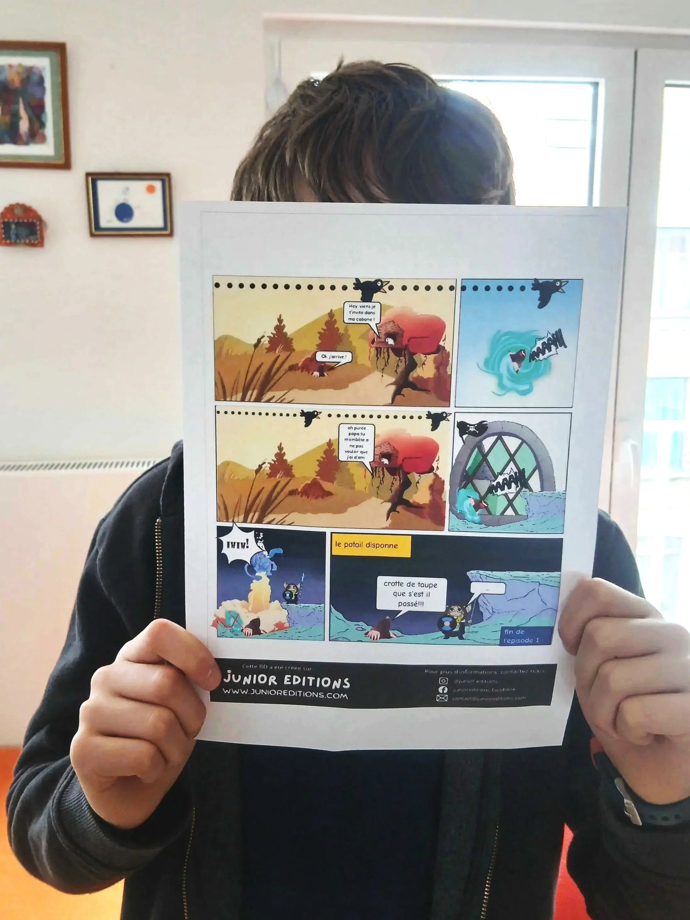 Un enfant tient une bande dessinée imprimée colorée devant son visage à la maison.