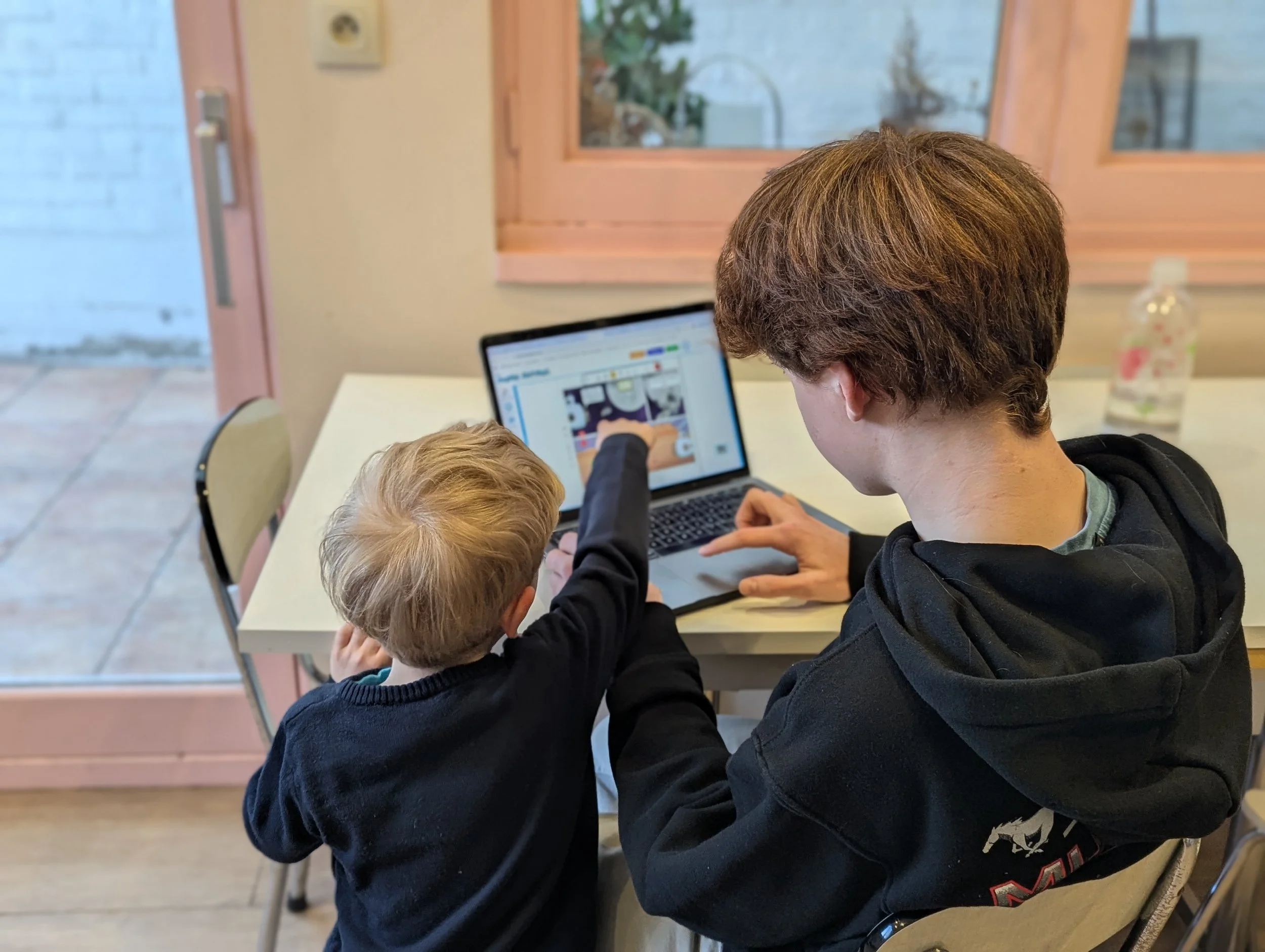 Travail d'équipe sur le studio de BD : deux enfants créent une histoire ensemble sur un ordinateur portable au bord d'une fenêtre.