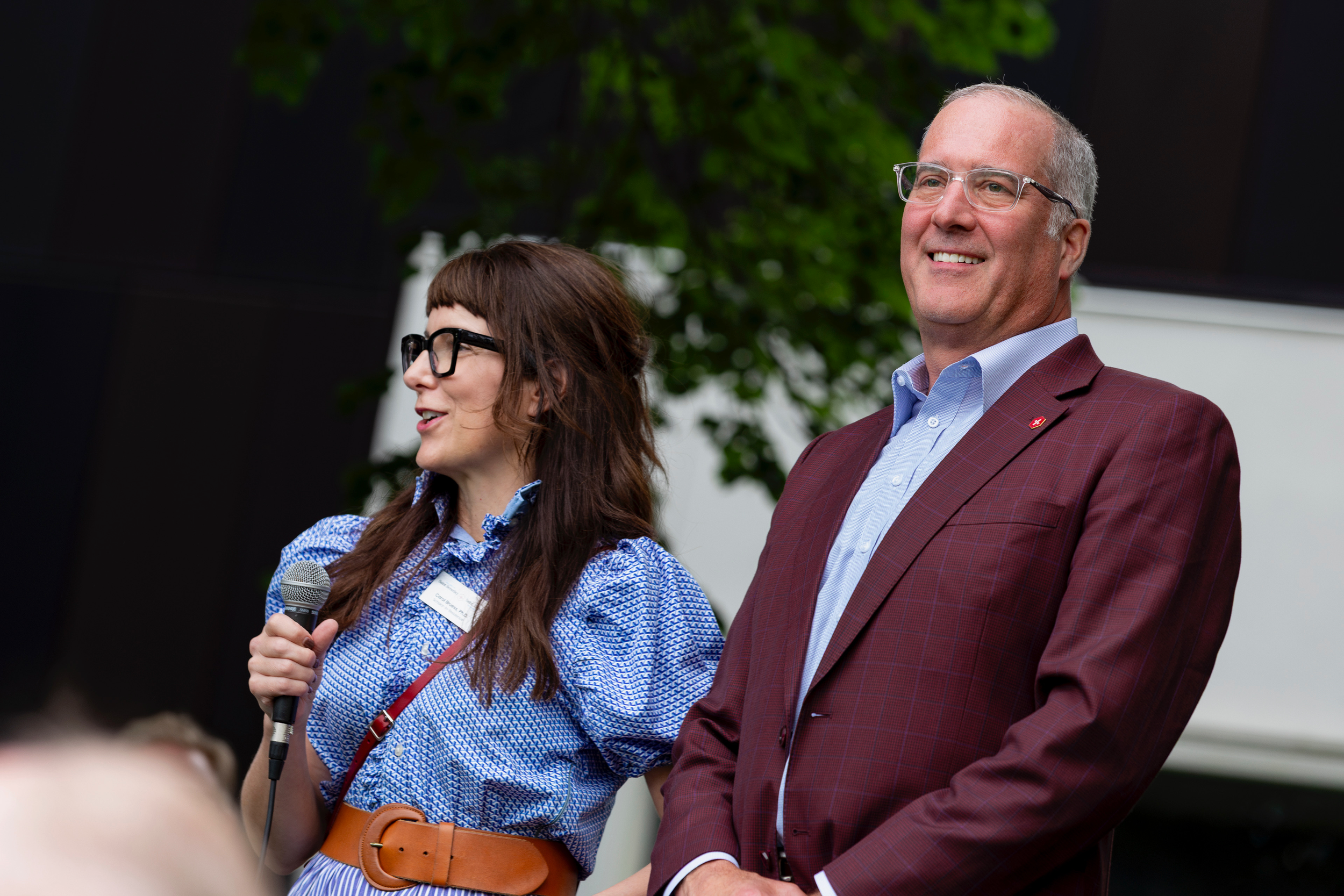 Carol Bruess holding a microphone standing next to Brian Bruess