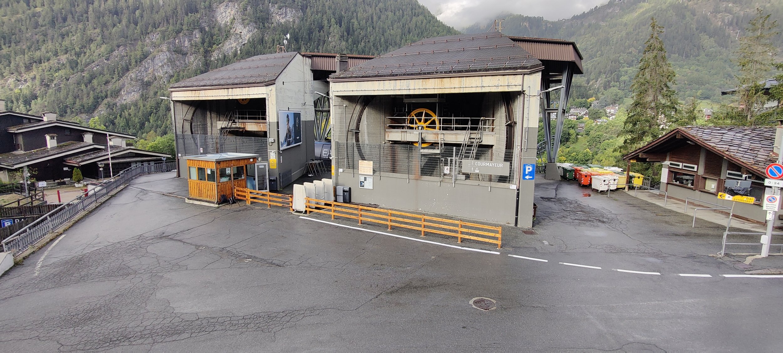 Immagine di una funicolare o funivia in stile montano in un villaggio alpino con case in legno e montagne sullo sfondo, giorno nuvoloso.