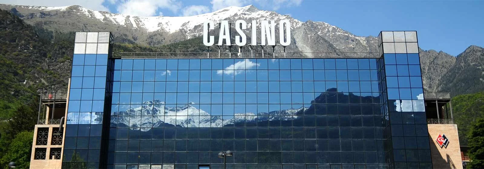 Edificio con vetrate riflettenti che mostra le montagne nevose sullo sfondo e la scritta 'CASINO' in alto.