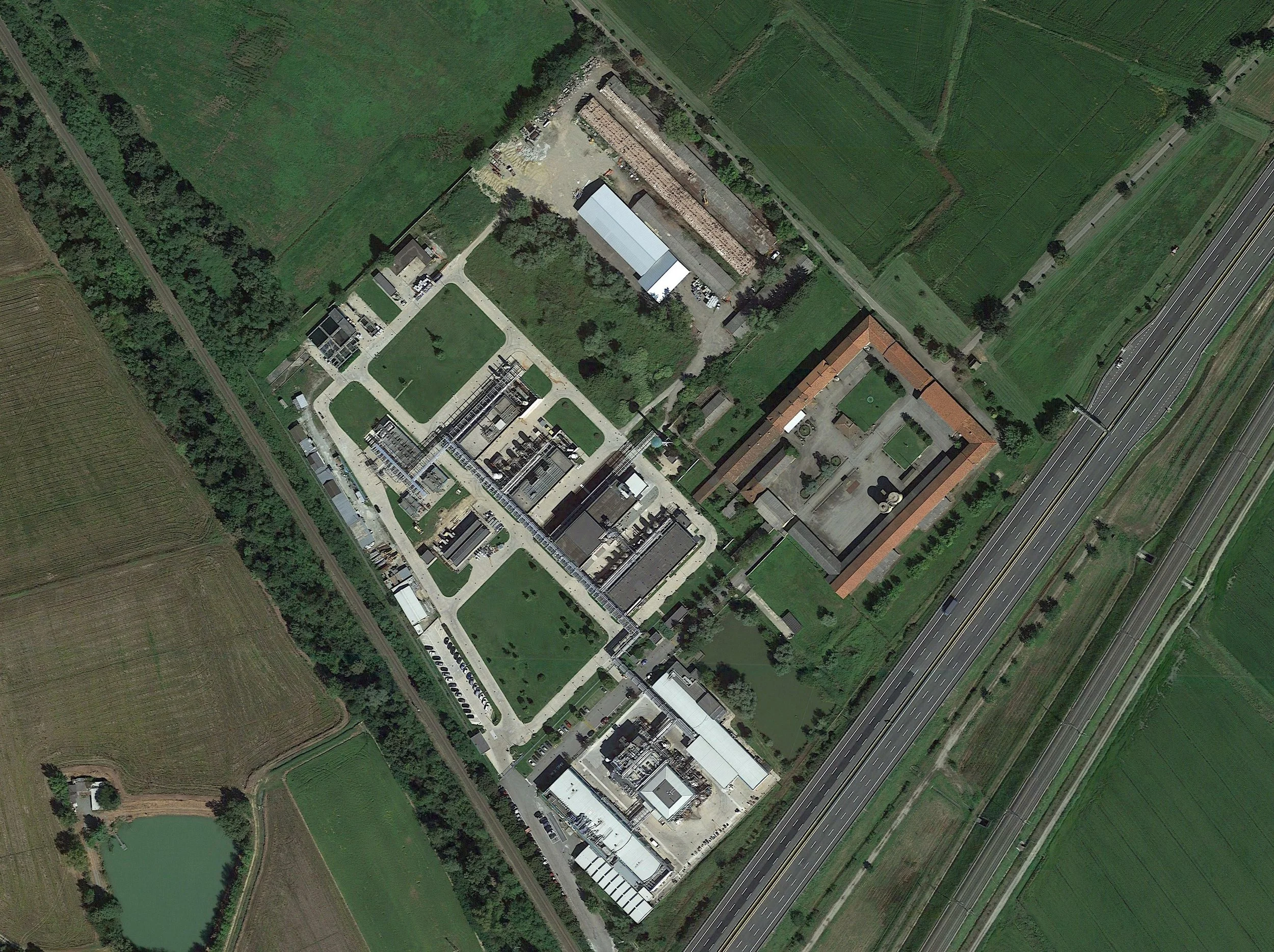 Vista aerea di un'area industriale circondata da campi verdi e un’autostrada vicina.