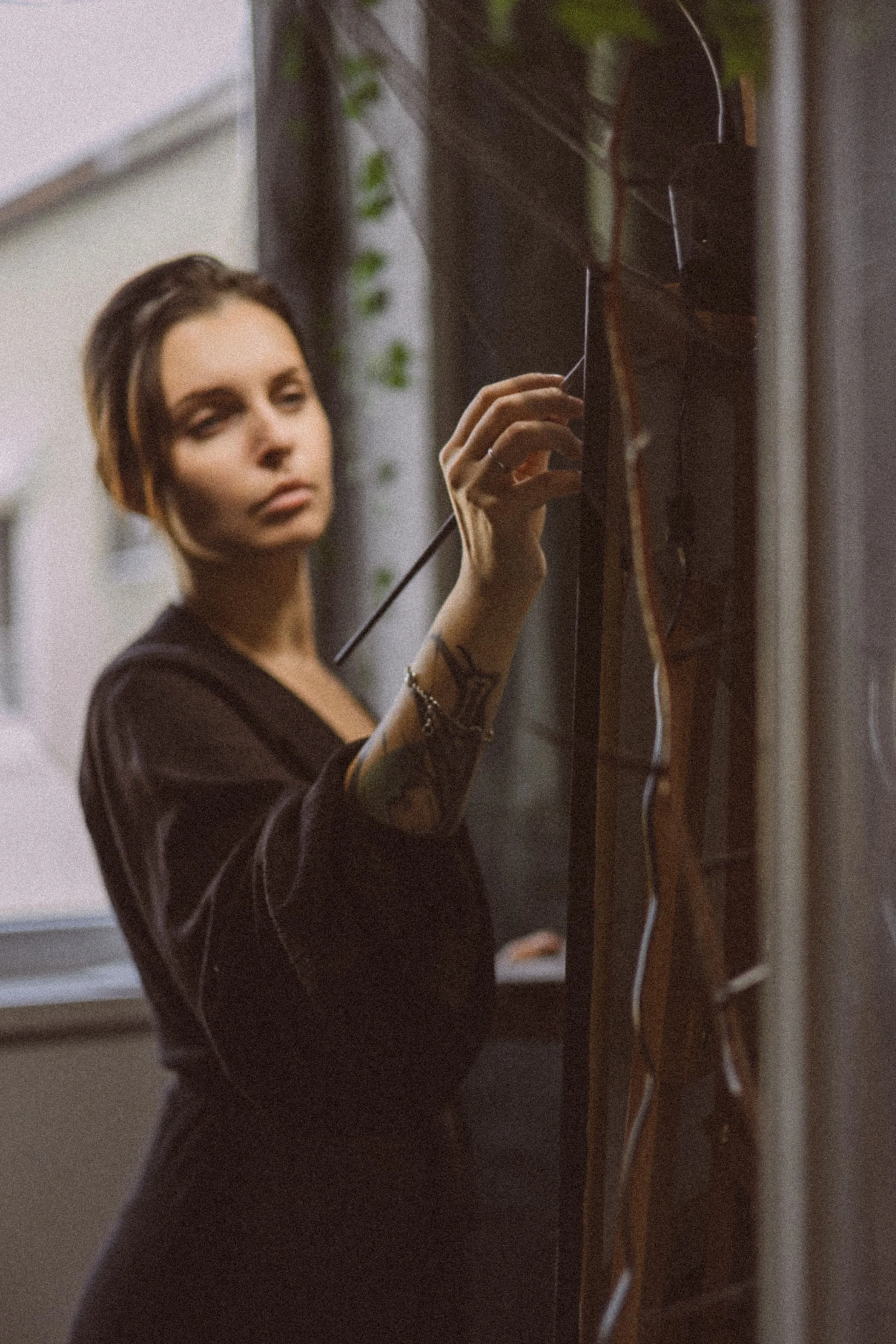 A woman with short, dark hair and tattoos on her arm is standing in front of a dark wooden panel with white wiring, and is looking at the panel as she adjusts or interacts with it.
