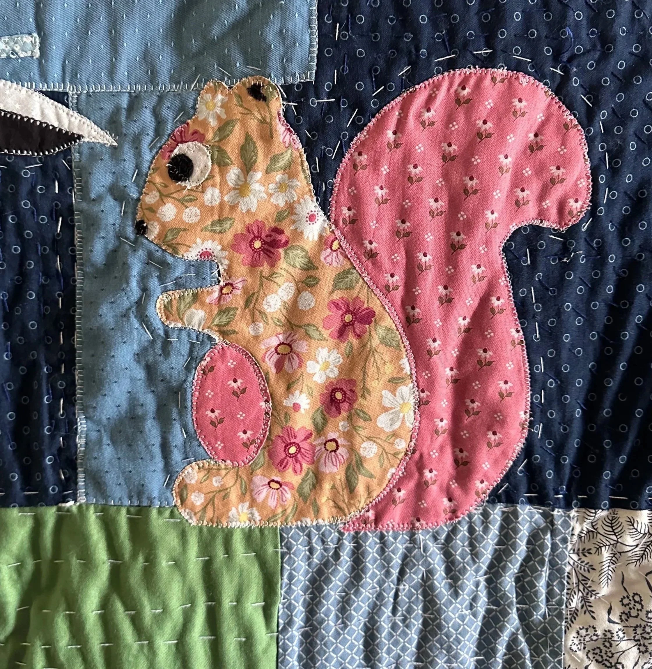 A quilt with various fabric patterns and colors, including a floral bear and a pink circle with small flowers.
