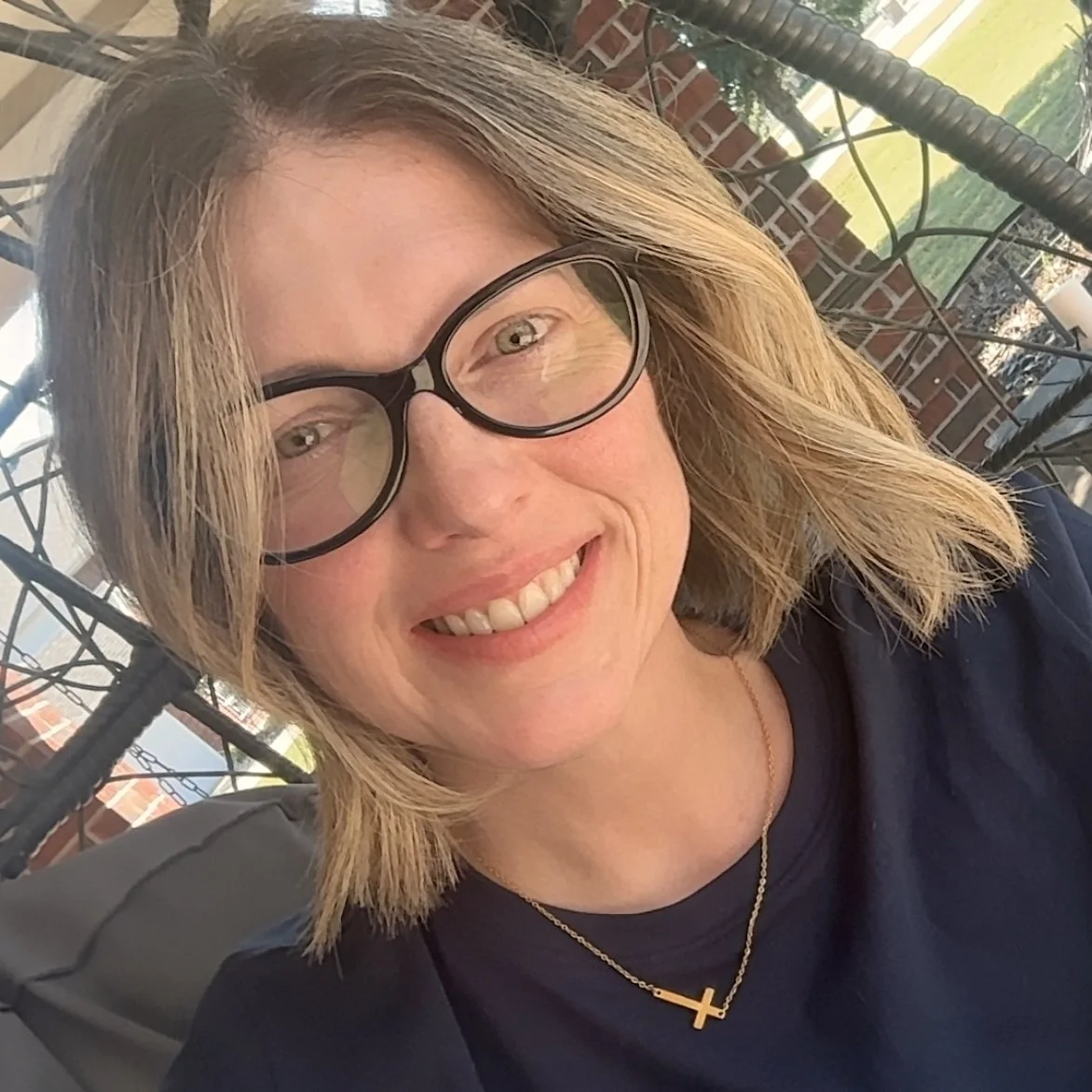 Marisa C. Gray., the author and creator of the Front Yard Friends, sitting in a chair on her porch in Texas, smiling.