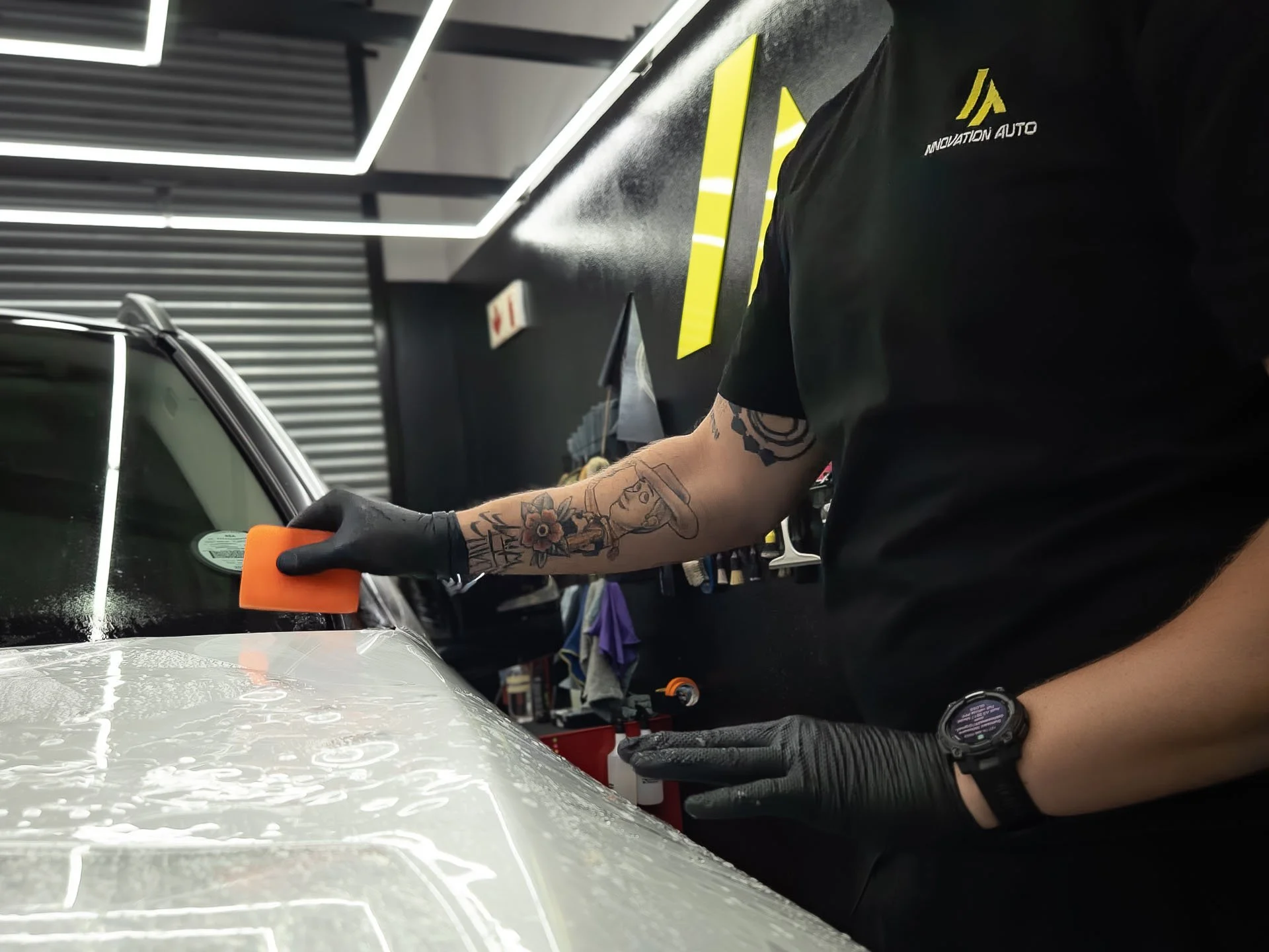 Hands squeegeeing paint protection film across a white car bonnet