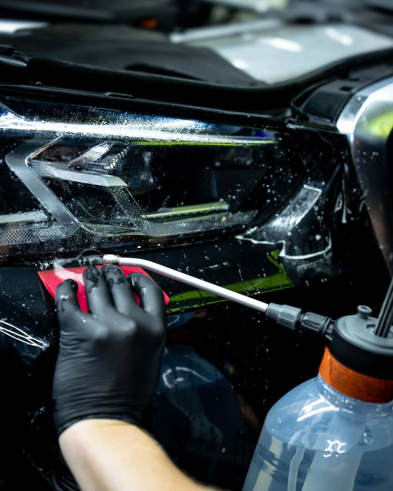 Close-up of a person in black gloves working on a car headlight with a tool during repair or modification process, with a water bottle in the foreground.