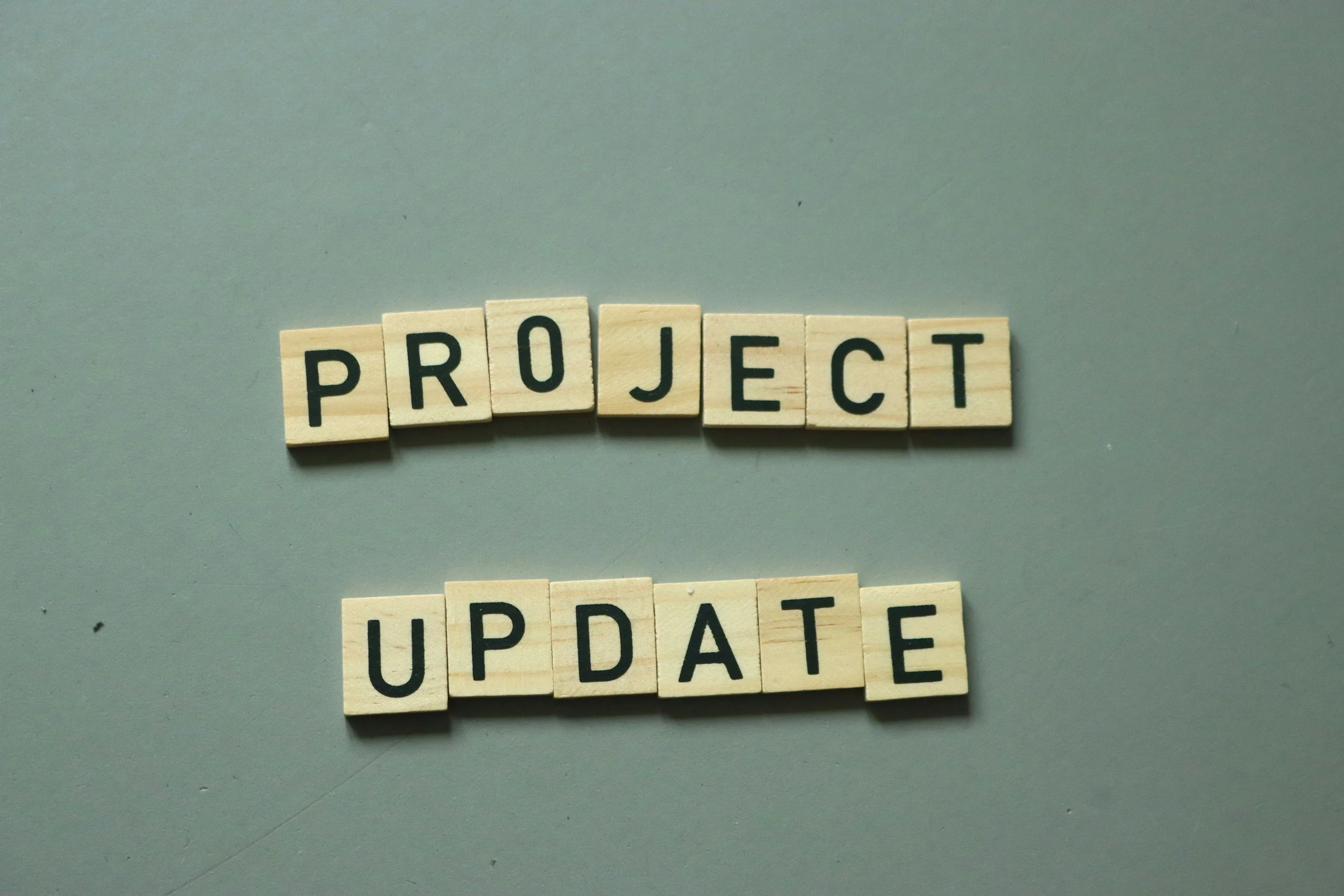 Wooden Scrabble tiles spelling out 'PROJECT' and 'UPDATE' on a gray background.