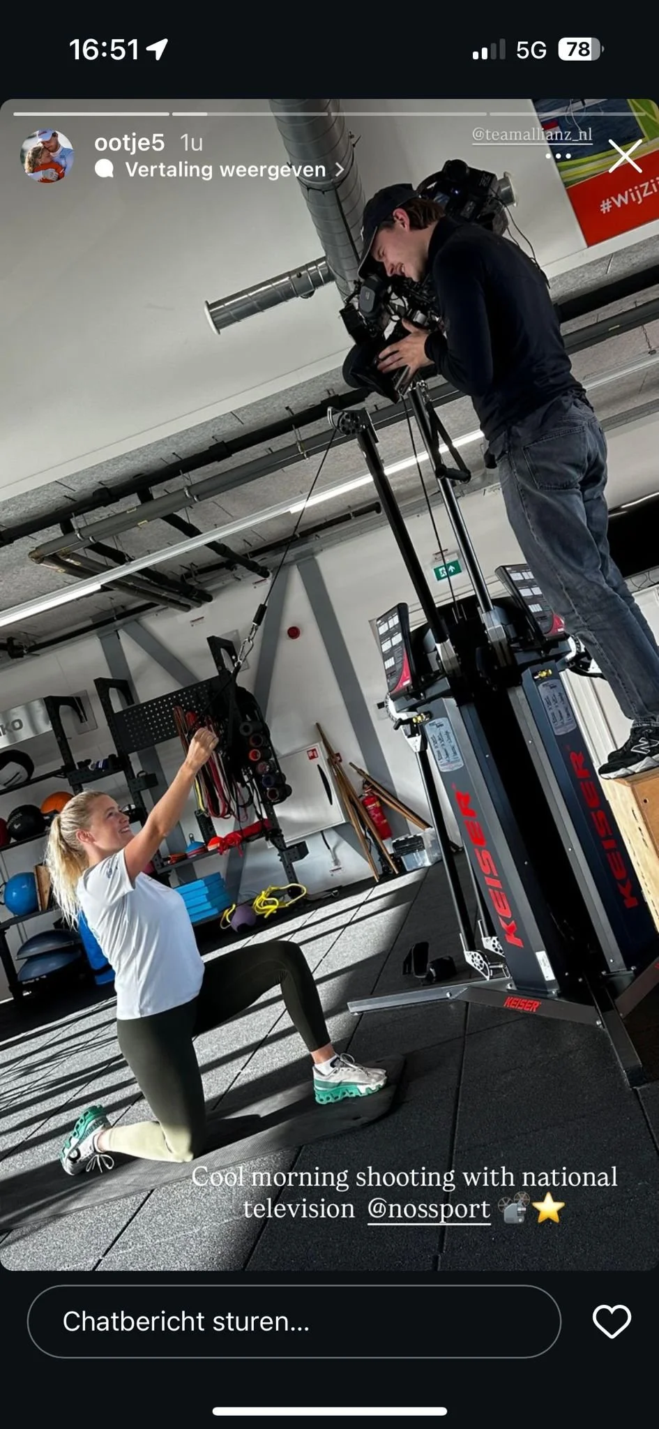 A woman in workout attire performing a lunge exercise on a treadmill while a man films her with a professional camera on a tripod in a gym. The gym has various equipment and weights on shelves in the background.
