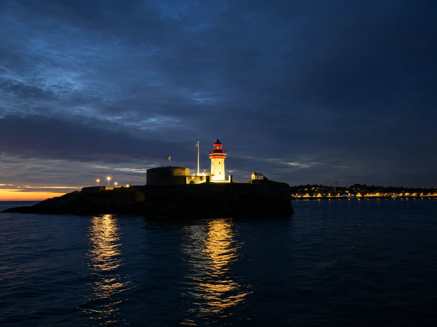 A lighthouse on a small island at dusk, with a dark sky, water reflecting the lighthouse lights, and distant city lights.