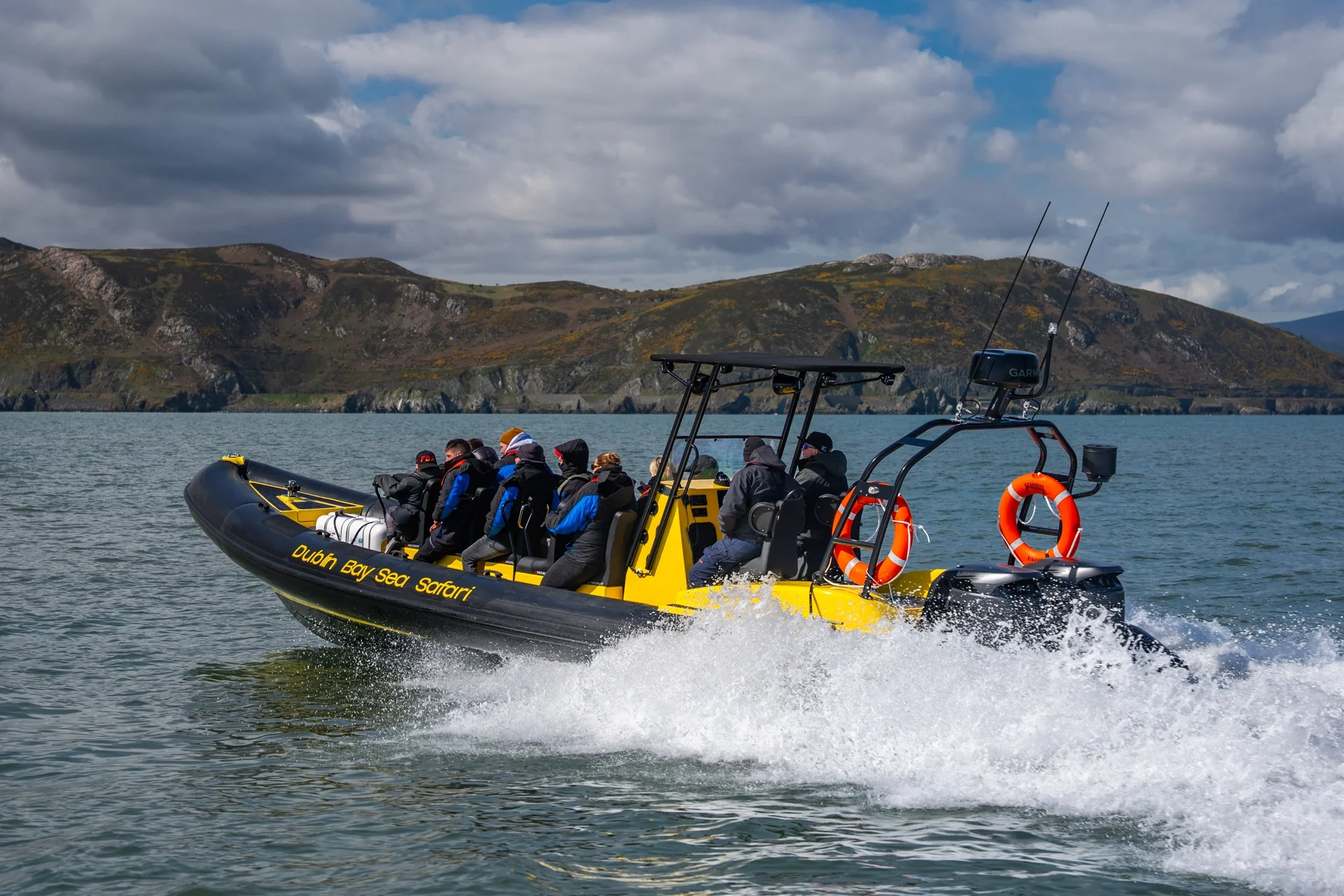 A RIB boat with multiple passengers wearing life jackets taking photos of Bray Head Co Wicklow with a fishing boat in the background
