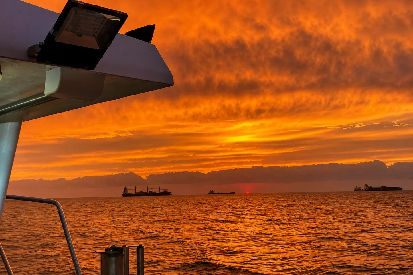 A sunset over the ocean with ships in the distance, viewed from the deck of a boat in Dublin Bay