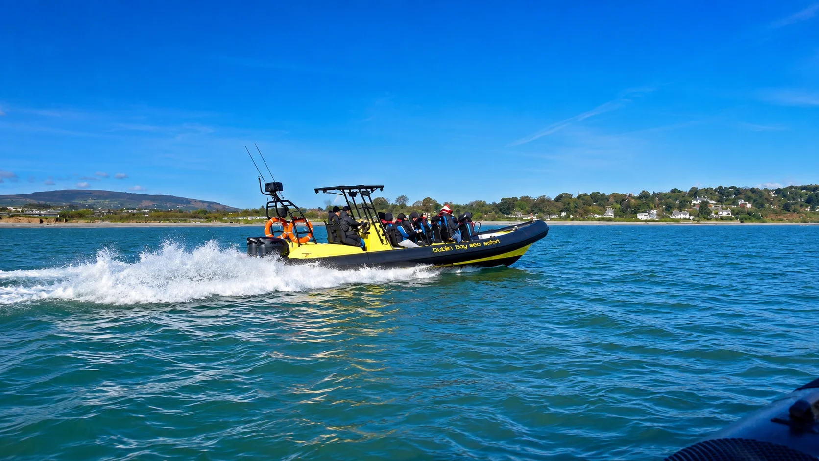 Yellow and black sea safari boat with passengers on the water, wearing life jackets and hats, near the coast on a sunny day.