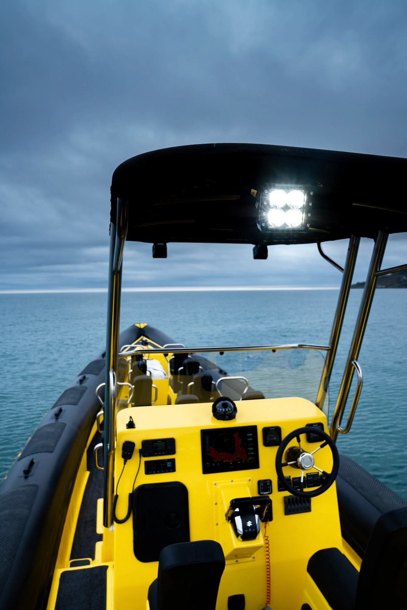 Inside view of a yellow Dublin Bay Sea Safaris boat with navigation and communication equipment, steering wheel, and bright LED light, on calm water with an overcast sky.