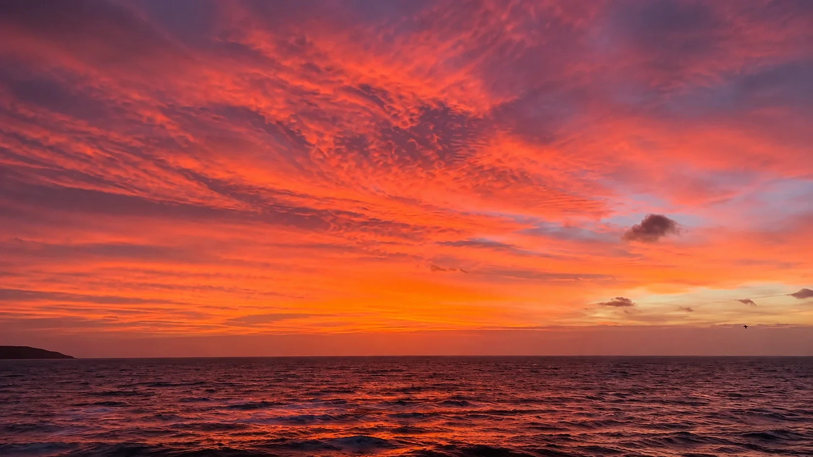 Sunset over Dublin Bay with colourful pink, purple, and orange clouds in the sky and gentle waves on the water.